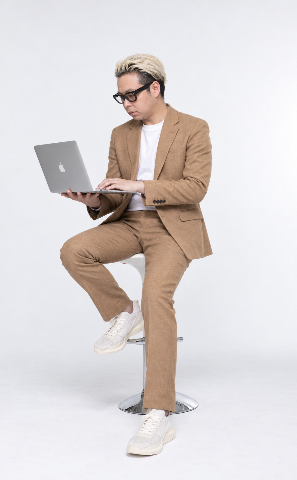 キャメル色のジャケットと白いTシャツ姿で、座ってMacを操作する柏原教継の人物イメージ